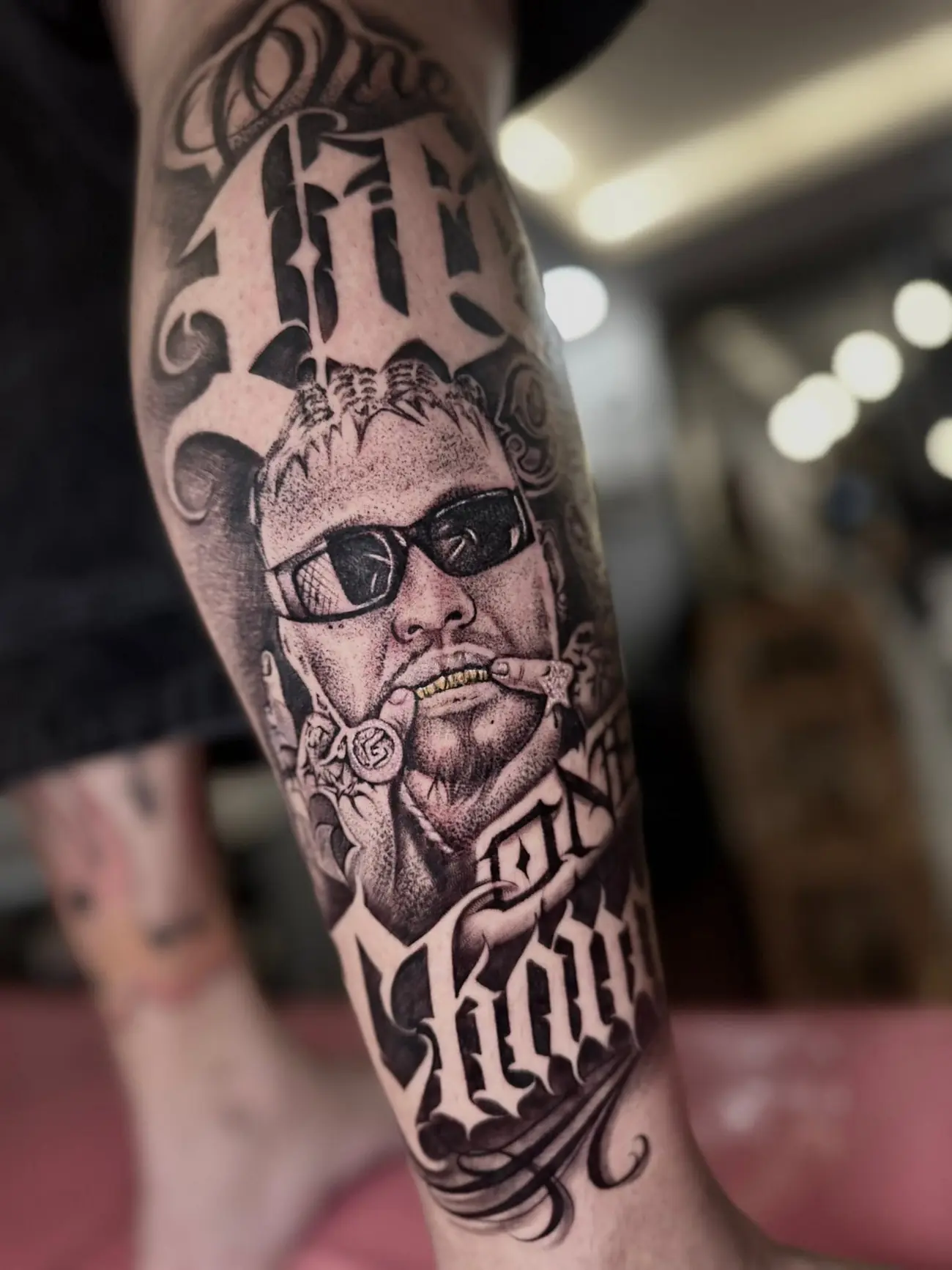 Black and grey chicano lettering and a smoking portrait on a forearm