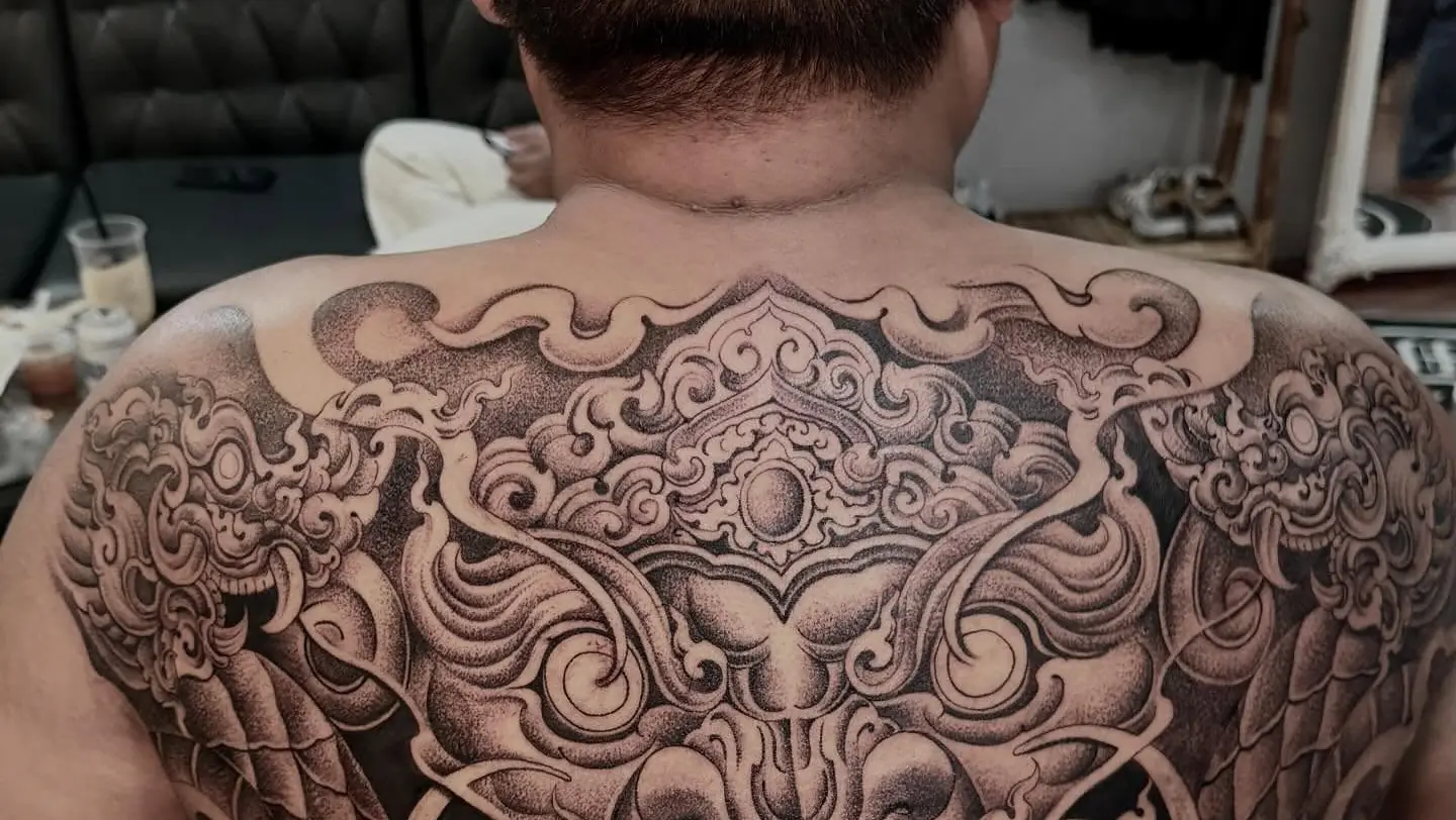 A large Khmer kala face wrapped in kbach cloud scrollwork, tattooed across a client's whole upper back by Meng