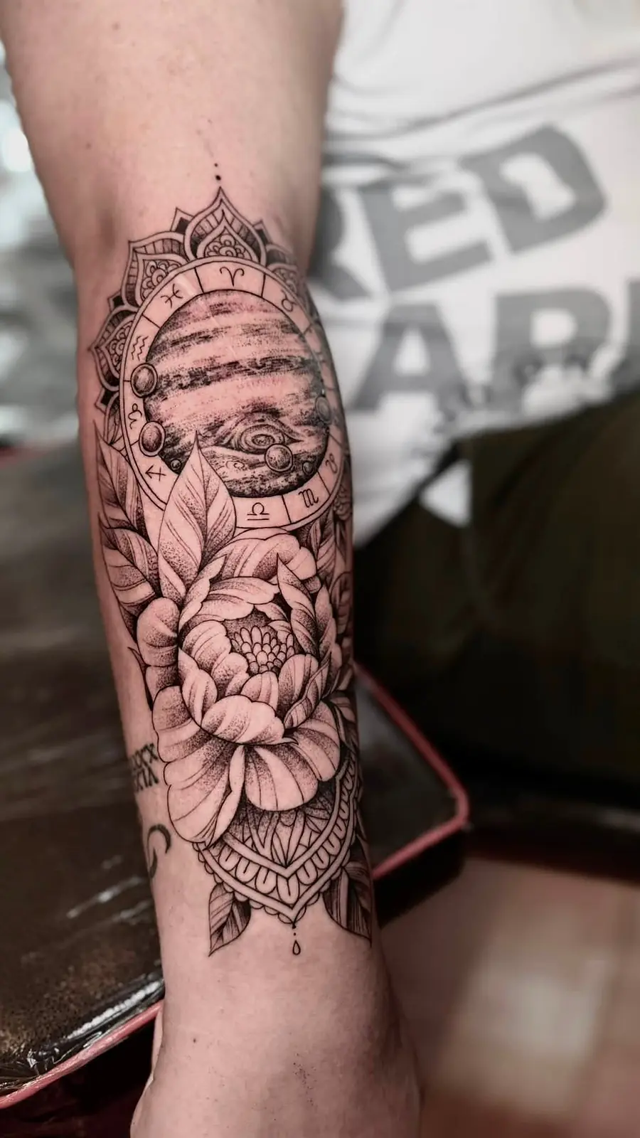 An ornamental mandala with a peony and an eye in fine dotwork on a forearm