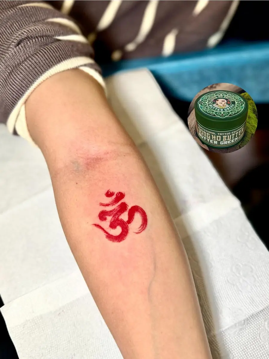 A small red ink character freshly tattooed on a forearm