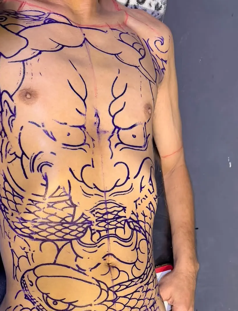 A client's torso and legs covered in violet stencil linework, mapping out a full bodysuit before any ink goes in