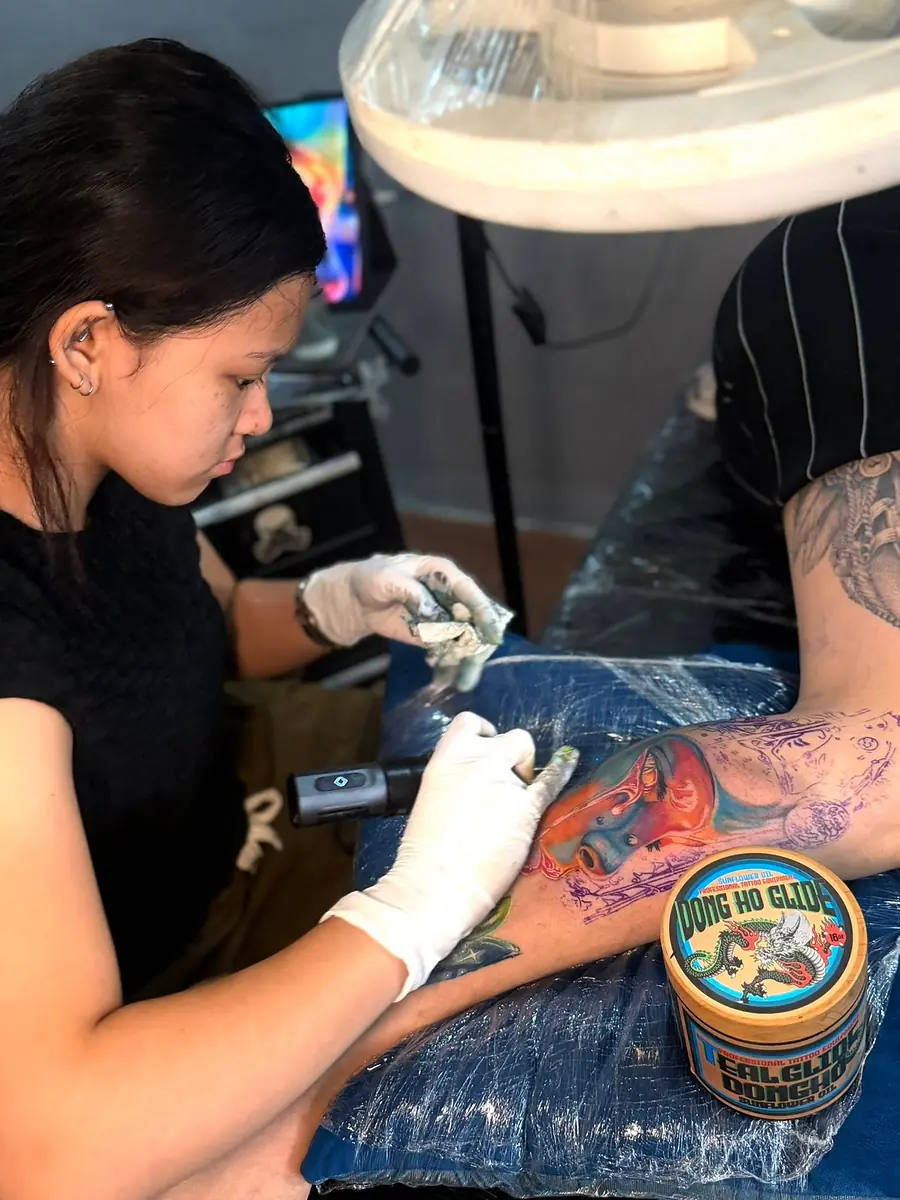 An artist at 55 Tattoo working colour into a client's arm sleeve