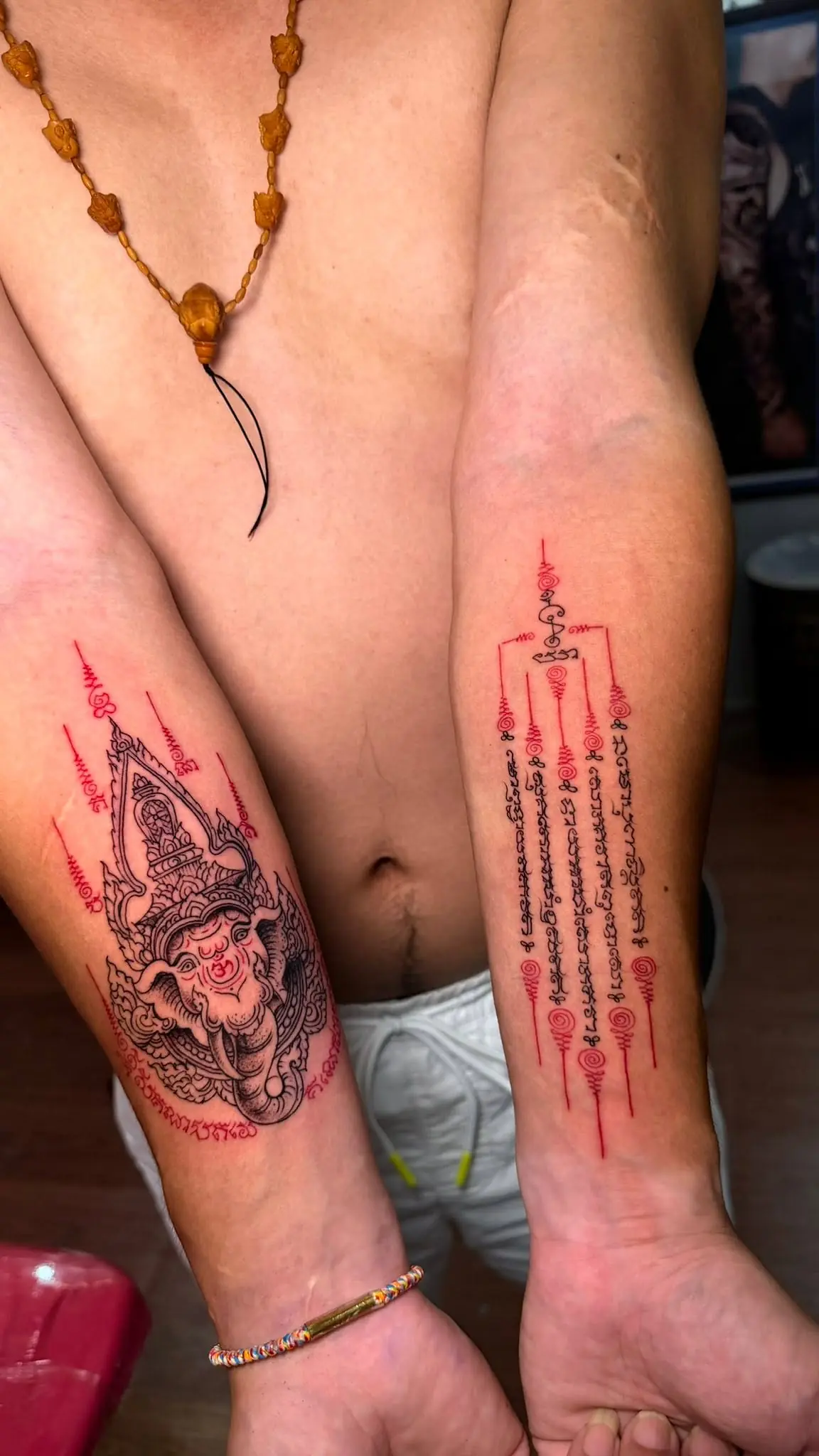 Sacred Khmer yantra in red down one forearm, a black kala guardian on the other